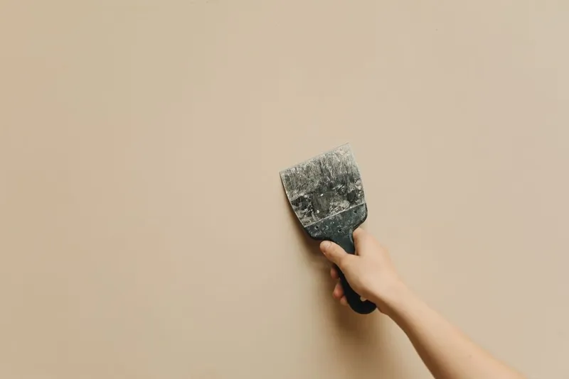 Hand met spaan tegen een gestucte wand